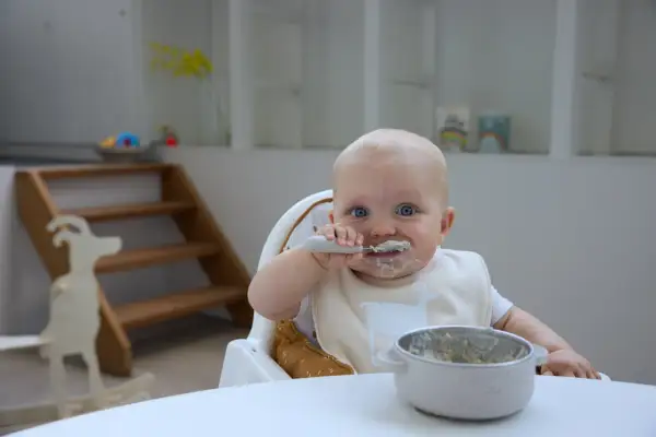 Ein süßer **Joghurt Baby** mit blauen Augen isst mit Löffel. Der Latz ist mit einer Ziege verziert.