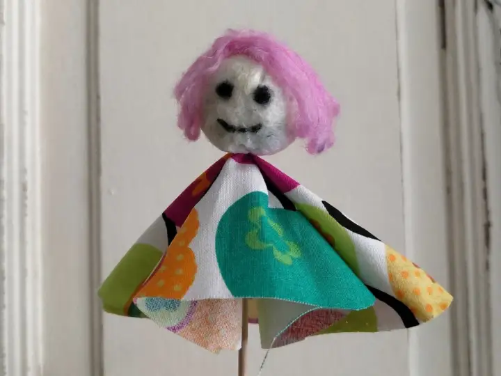 Eine selbstgemachte Puppe mit pinker Wolle als Haar und buntem Stoffkleid. Perfekt zum Filzen mit Kindern.